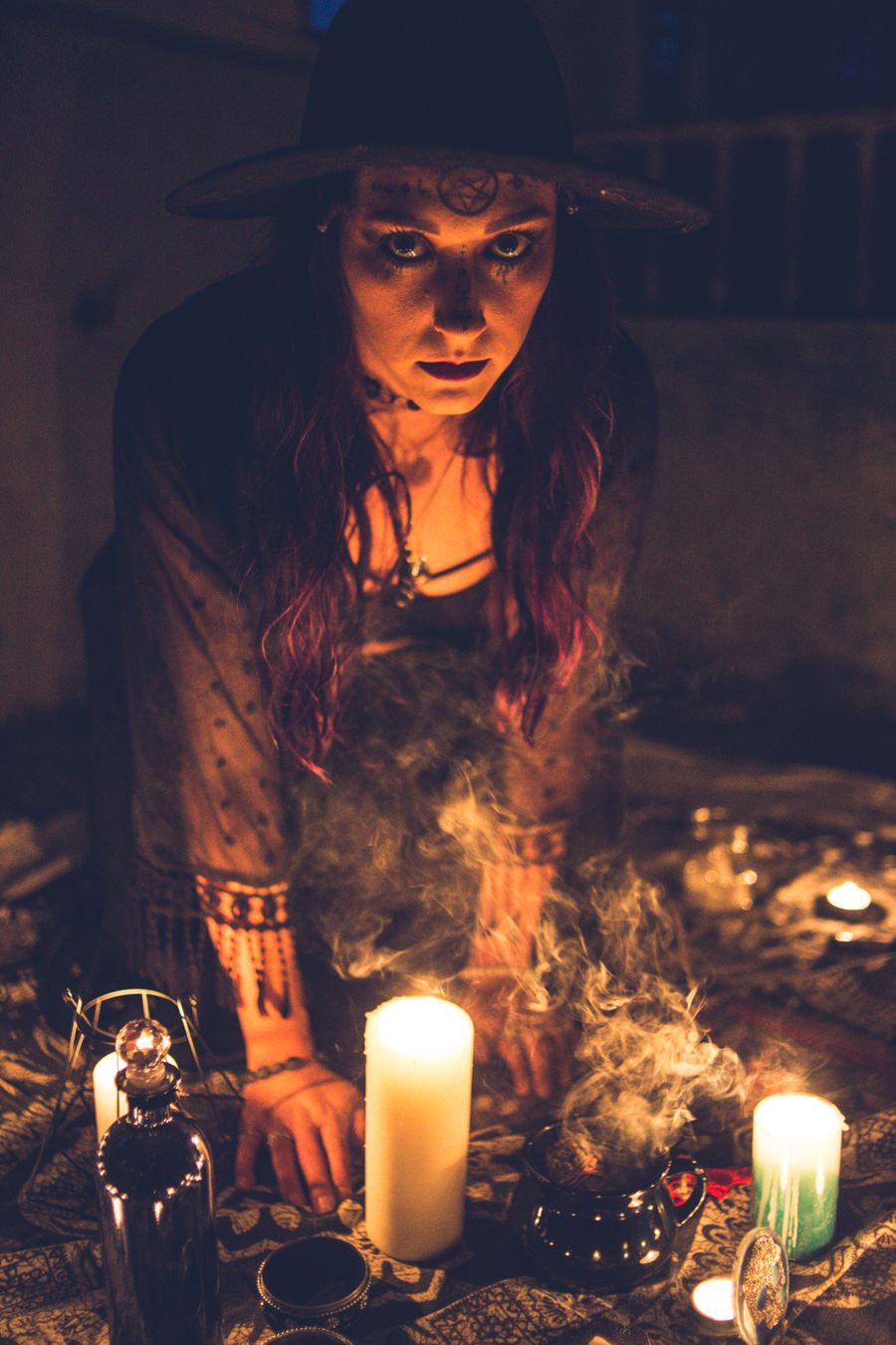 Mysterious woman in black hat gazes above burning candles and dark smoke